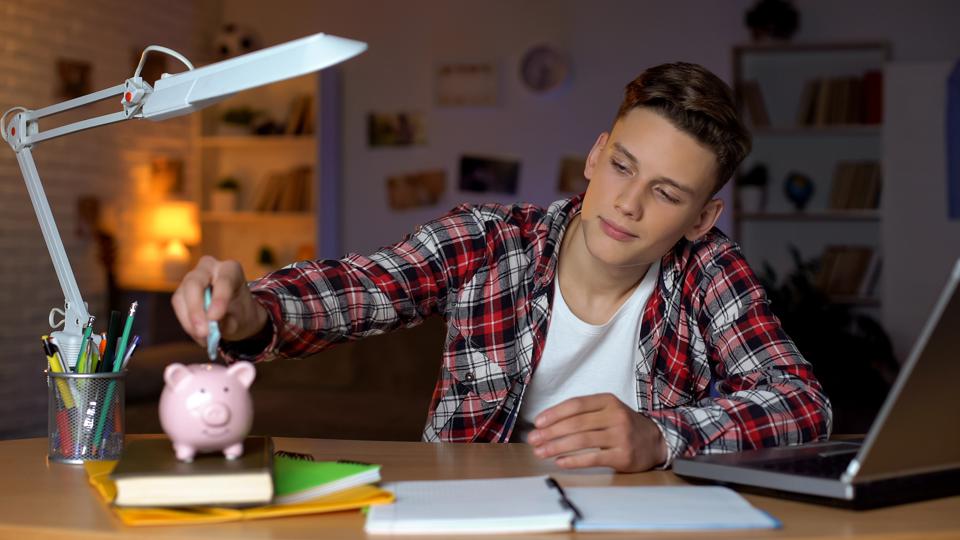 A teenager holding a euro banknote by putting it in a piggy bank, financial education