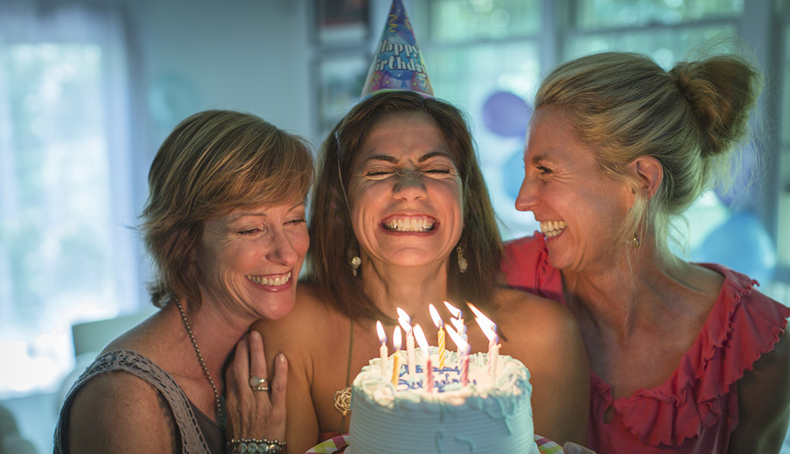 happy woman holding a birthday cake wishes a wish before she blows out the candles while two friends watch happy woman holding a birthday cake wishes a wish before she blows out the candles while two friends watch