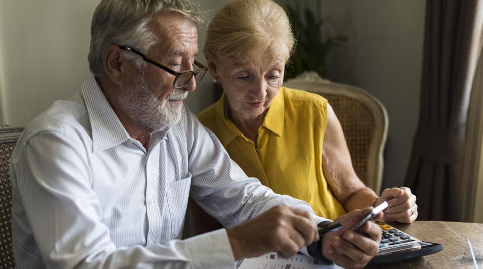 An older couple uses a calculator while filling out tax forms at the table.